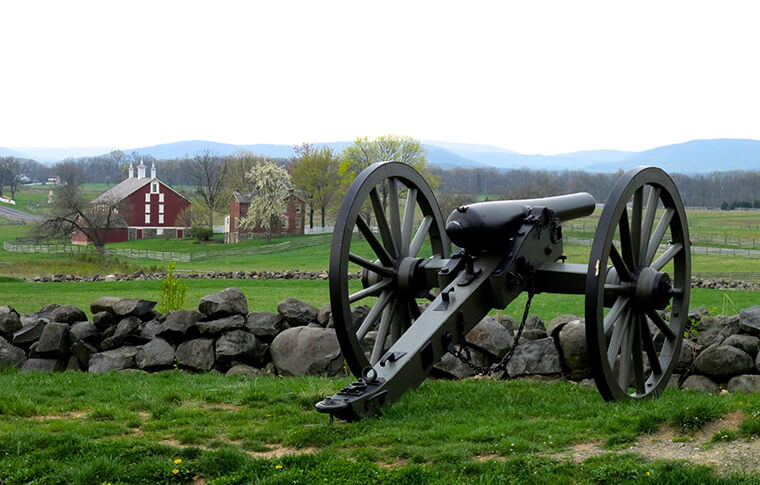 Antique cannon on an open field with a farmhouse in the far background